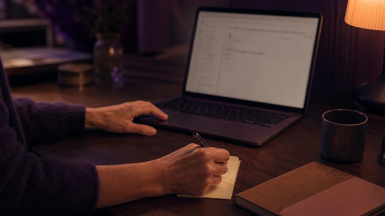 Mains notant une première phrase de mail à côté d’un ordinateur
